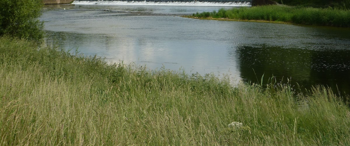 A river with a dam and a bridge in the background.