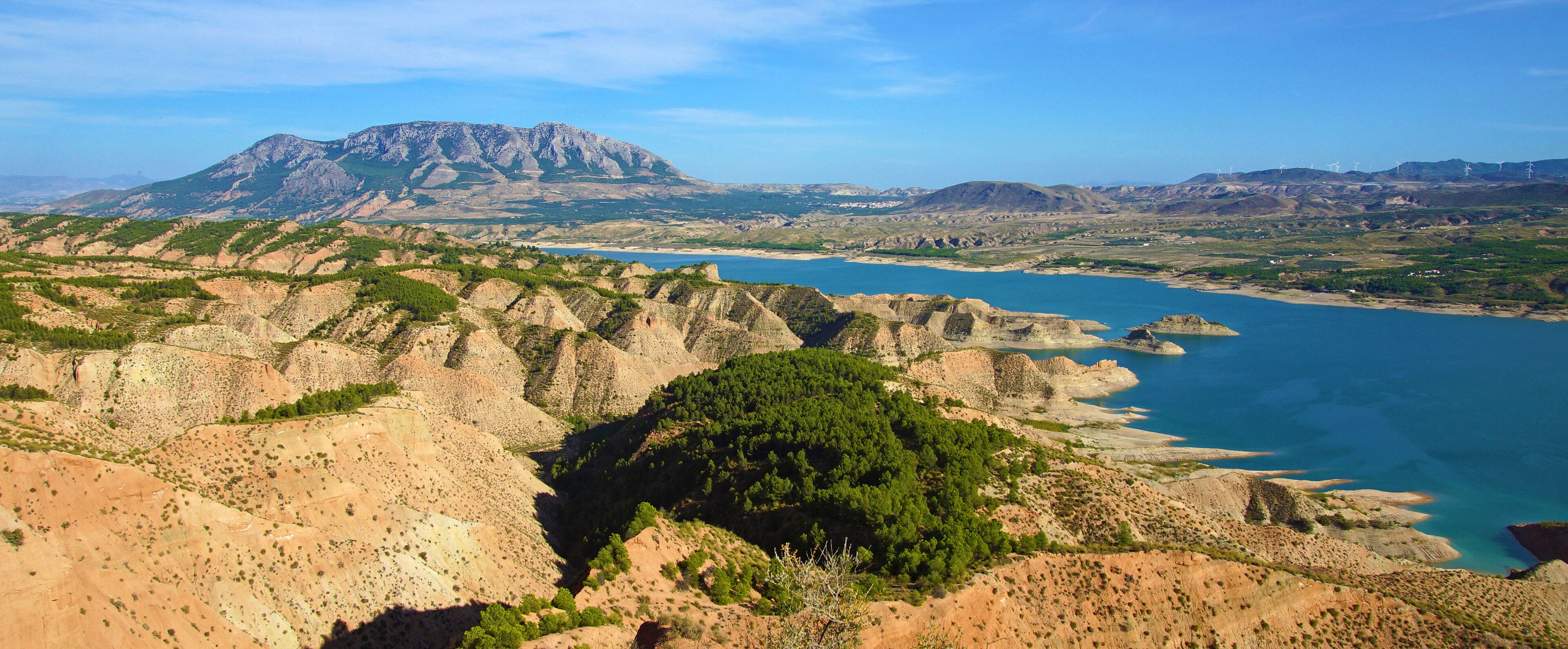 A mountainous landscape with a prominent peak, a coastal area with clear blue waters, and scattered vegetation.