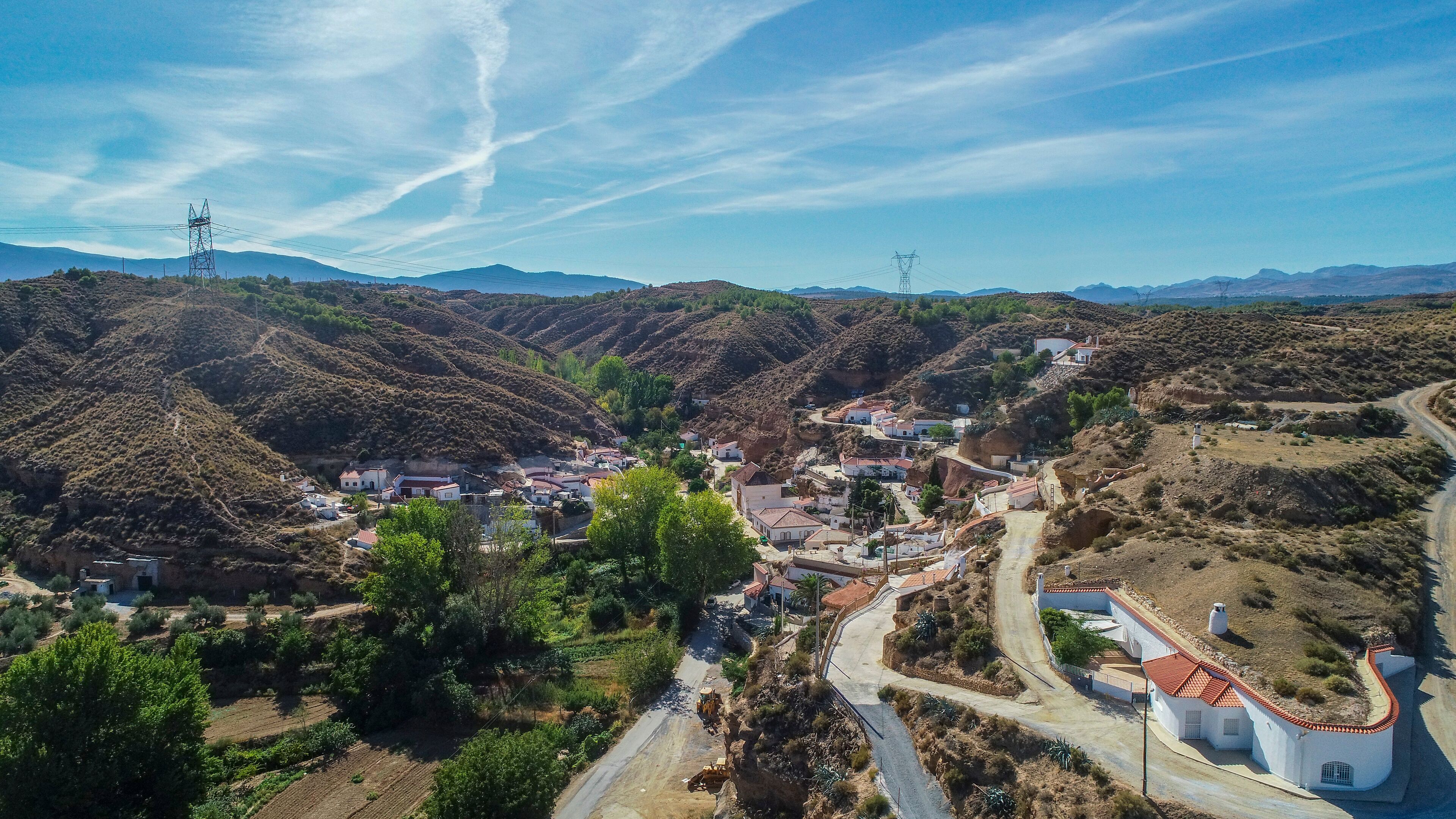 A mountainous village with terraced fields, a winding road, and power lines.