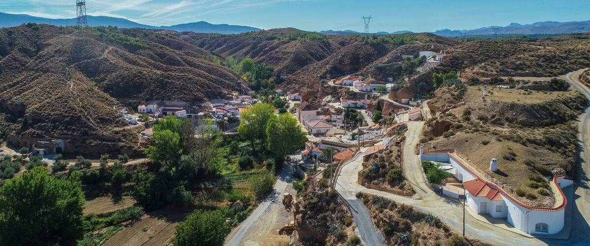 A mountainous village with terraced fields, a winding road, and power lines.