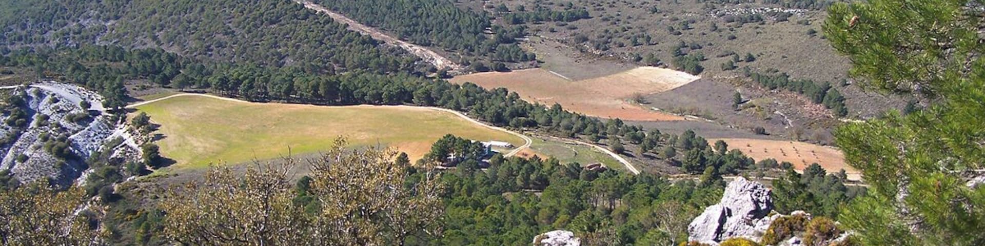 A mountainous landscape with a valley, a winding road, and scattered buildings.