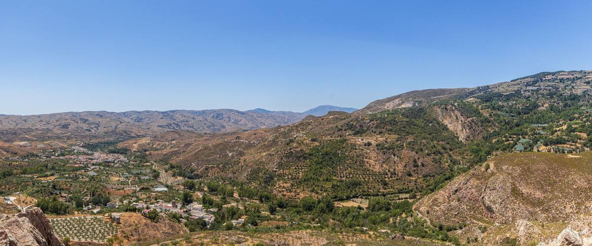 A mountainous landscape with winding roads, terraced fields, and scattered buildings.