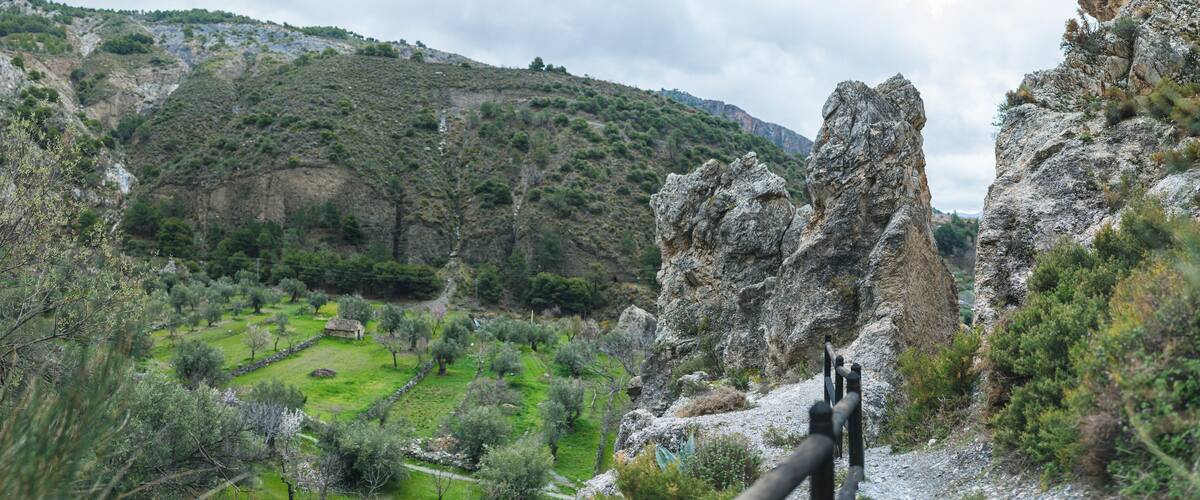 A mountainous landscape with rocky outcrops, a green valley, and a small building.
