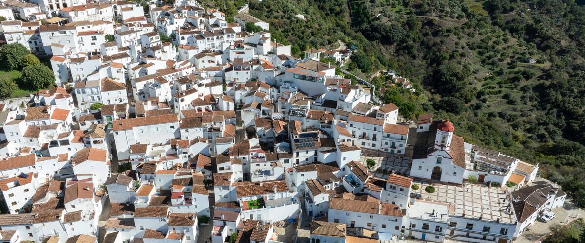 A densely packed white town with red-tiled roofs, surrounded by green hills.