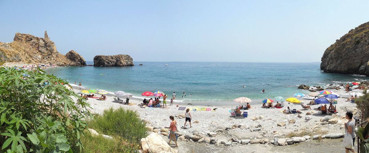 A beach with rocky cliffs, clear blue water, and colorful umbrellas.