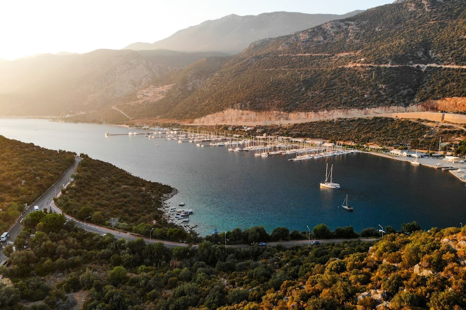 Un port de plaisance situé sur la côte, entouré de collines et bordé d’une route.
