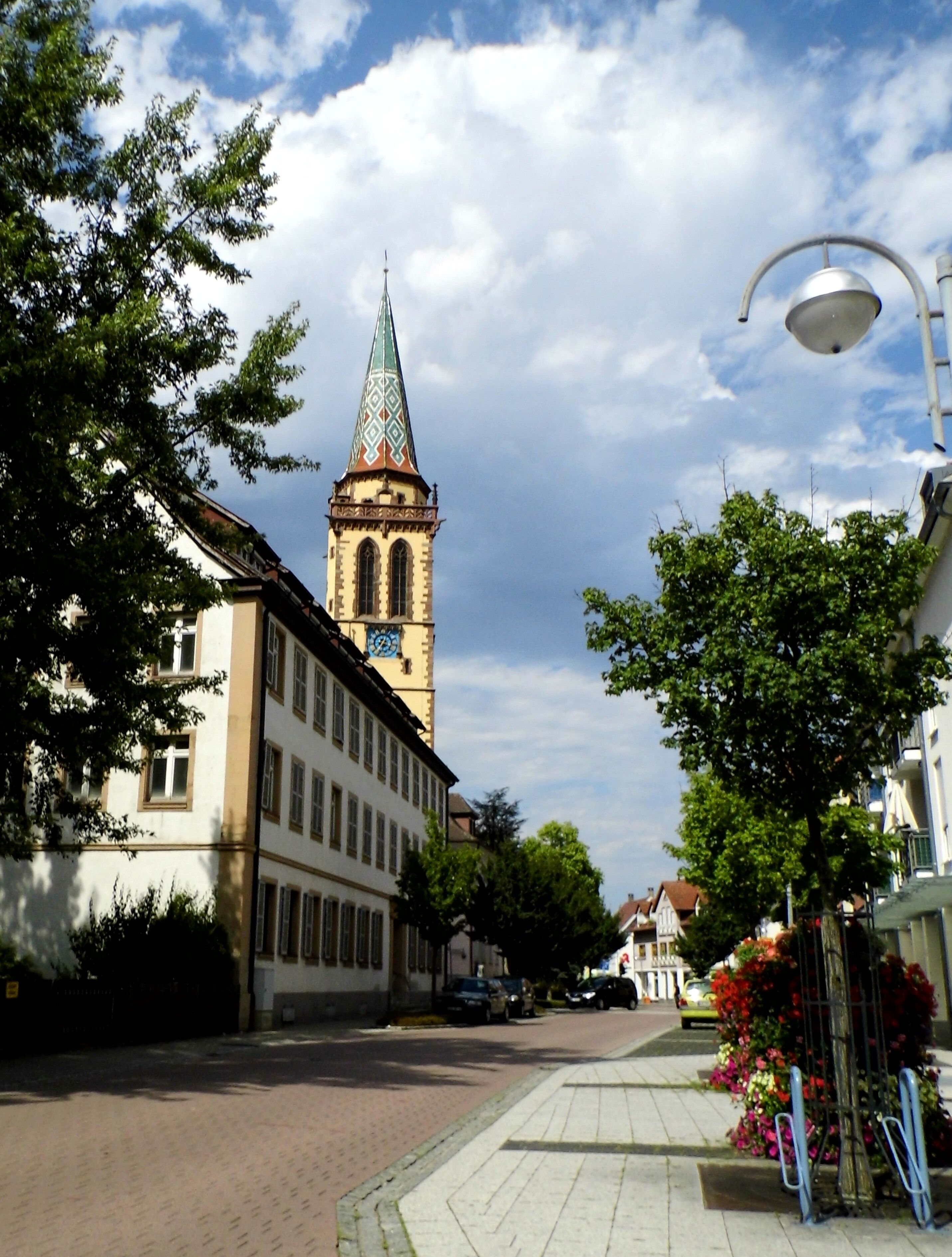 A street with a church tower, buildings, and trees.