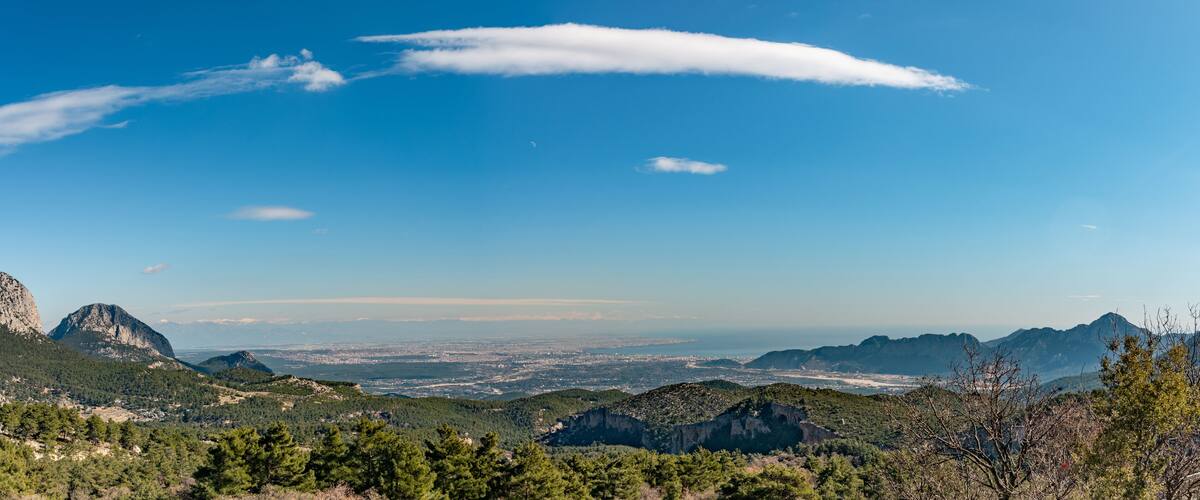 A mountainous landscape with a clear blue sky, distant cityscape, and prominent rocky peaks.