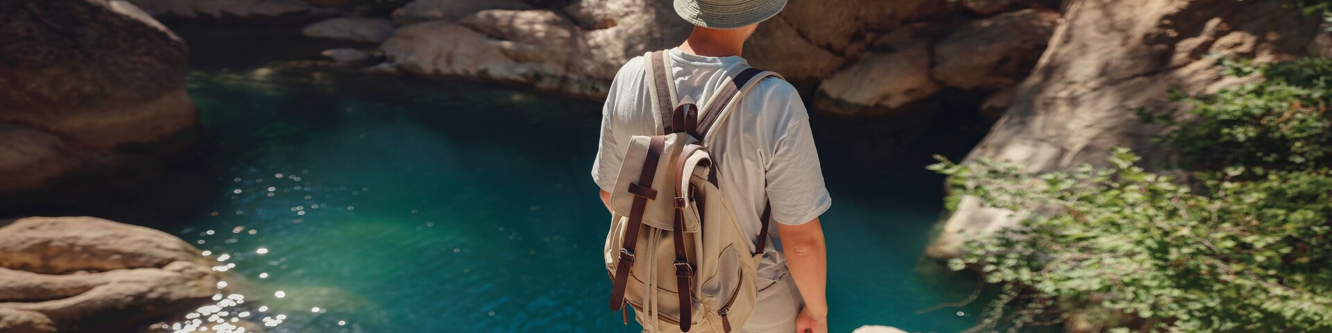 Una persona de pie sobre una roca junto a una piscina azul cristalina, rodeada de rocas y vegetación.