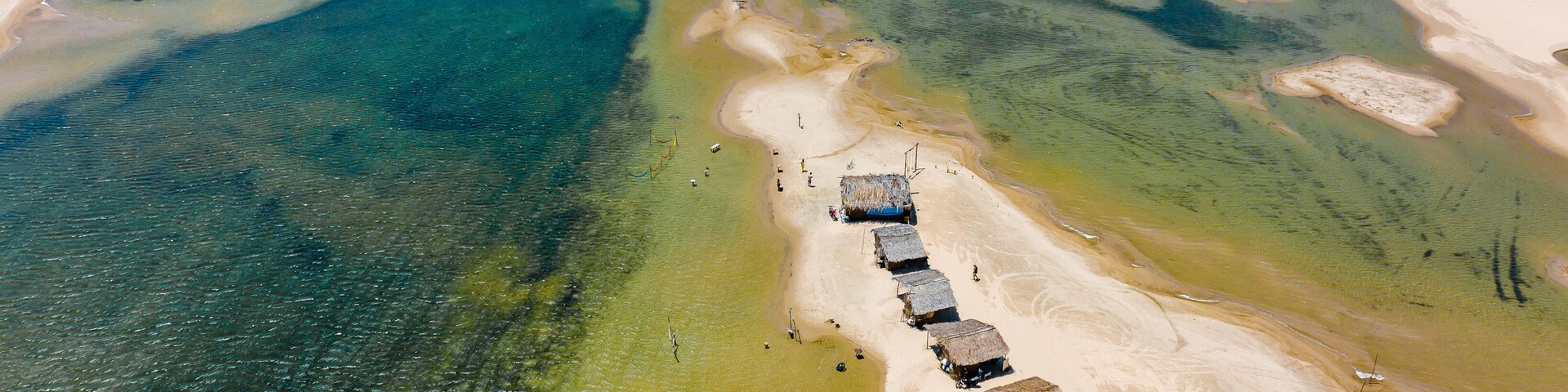 Vista aérea de uma área costeira com águas claras, praias de areia e uma fileira de cabanas com telhado de palha.