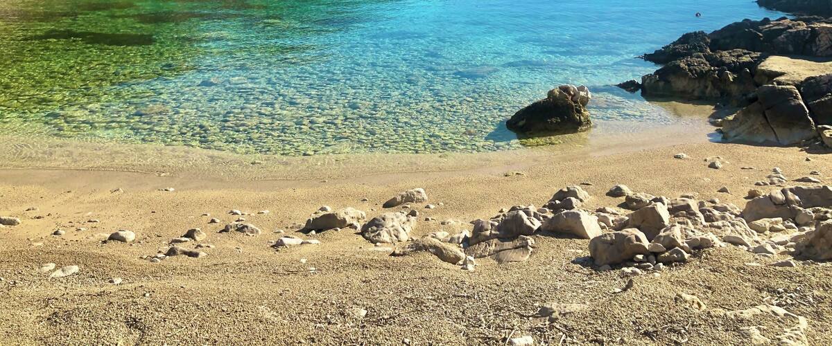 A clear lake surrounded by rocky shores and green hills.