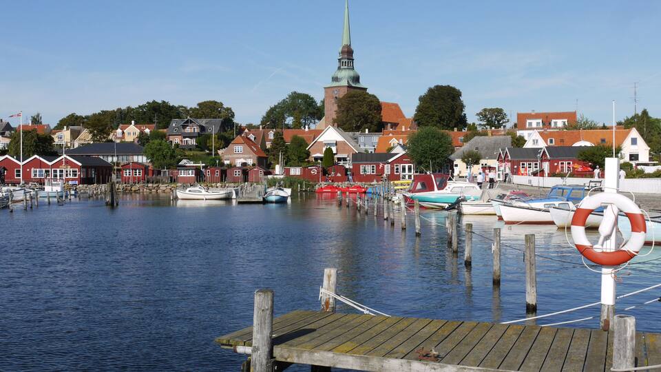 A harbor with boats, a church spire, and red houses.