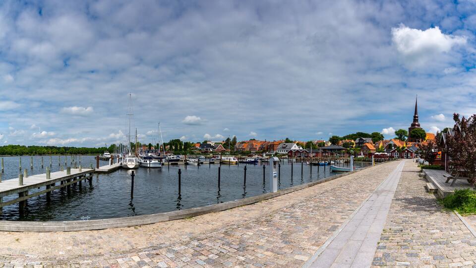 A harbor with boats, a cobblestone path, and a church with a tall steeple.