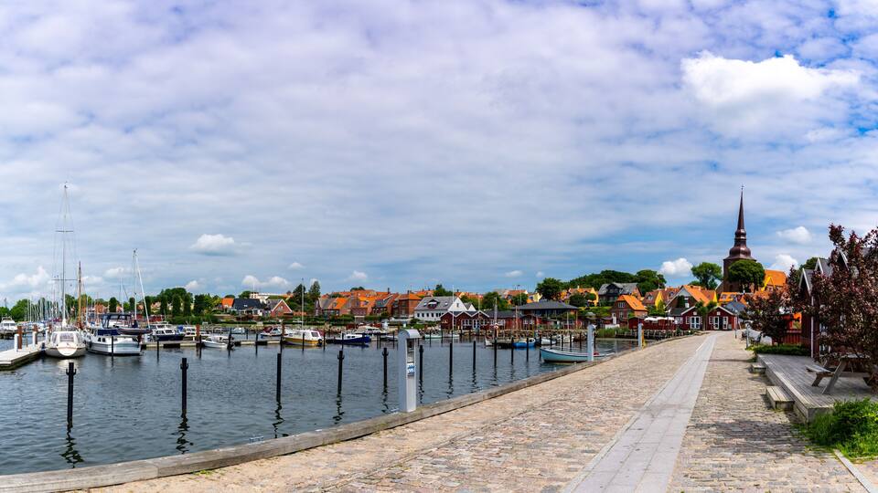 A harbor with boats, a cobblestone path, and a church with a tall steeple.