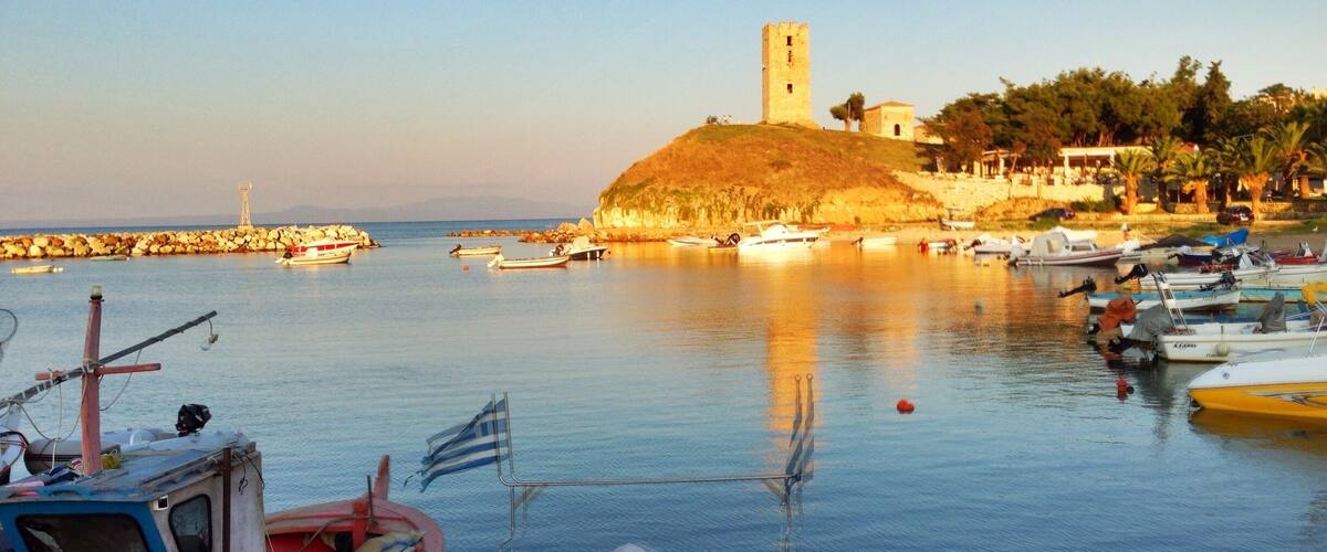 A harbor with boats, a lighthouse, and a castle on a hill.