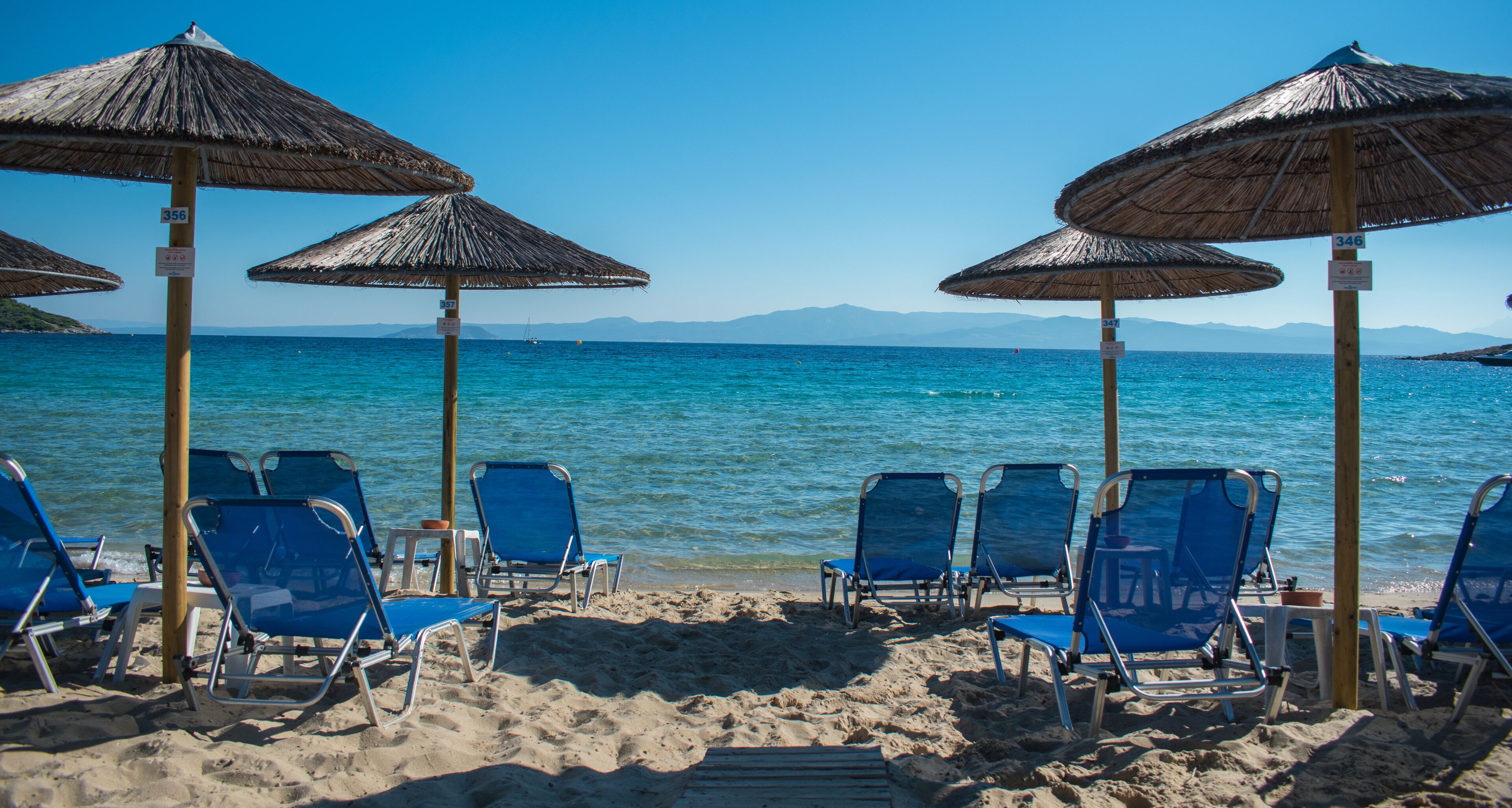 A beach with blue chairs and straw umbrellas.
