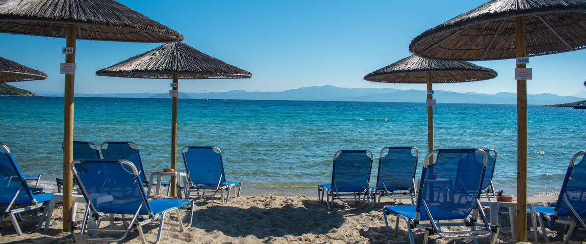 A beach with blue chairs and straw umbrellas.