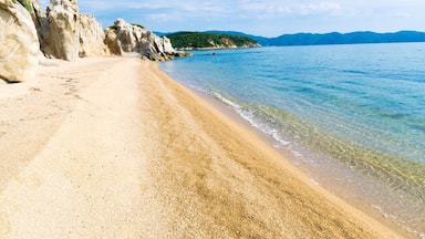 Una playa arenosa con agua cristalina, acantilados rocosos y colinas verdes al fondo.