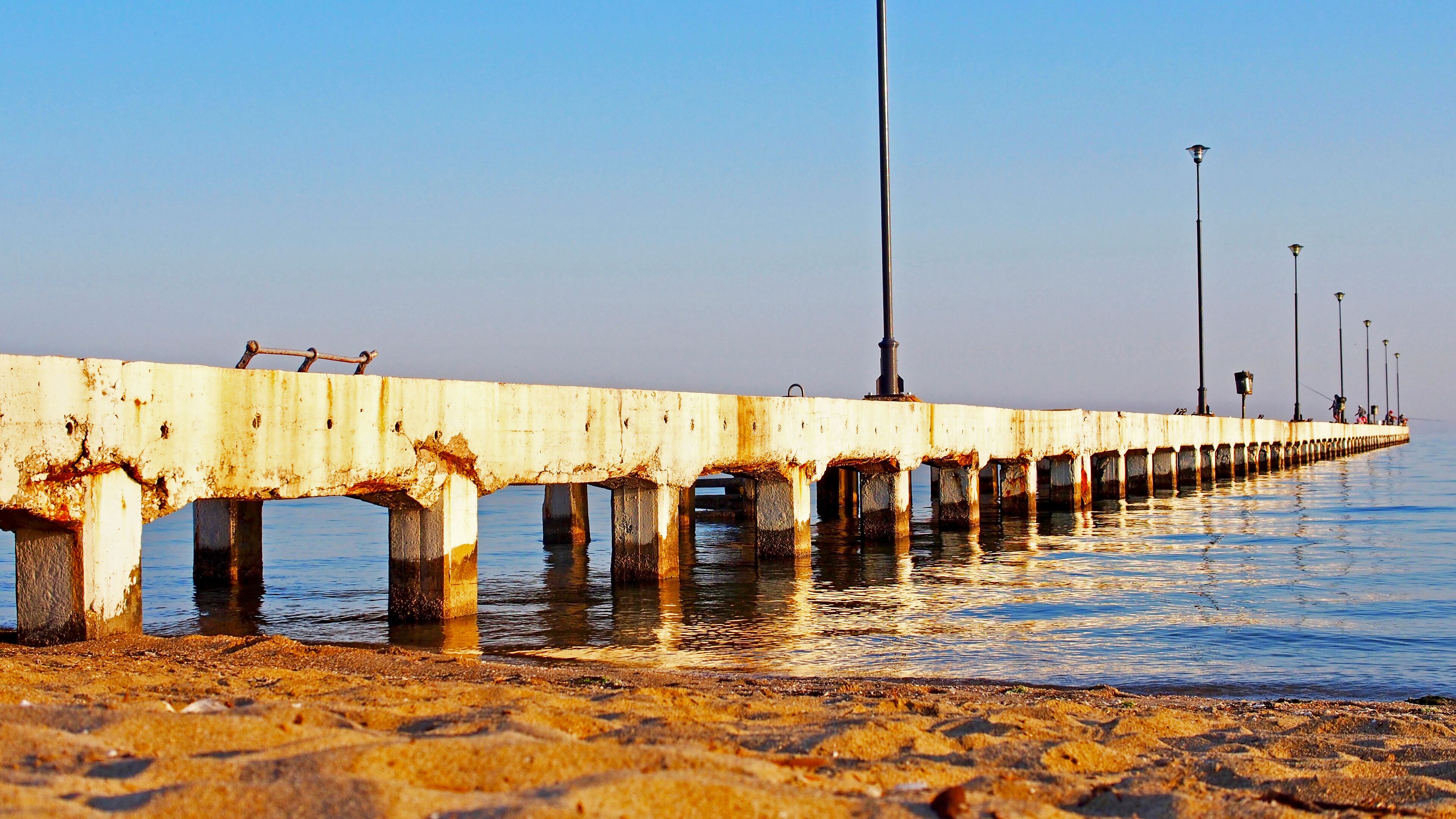 A long, rusted pier extending into calm waters with a clear sky.