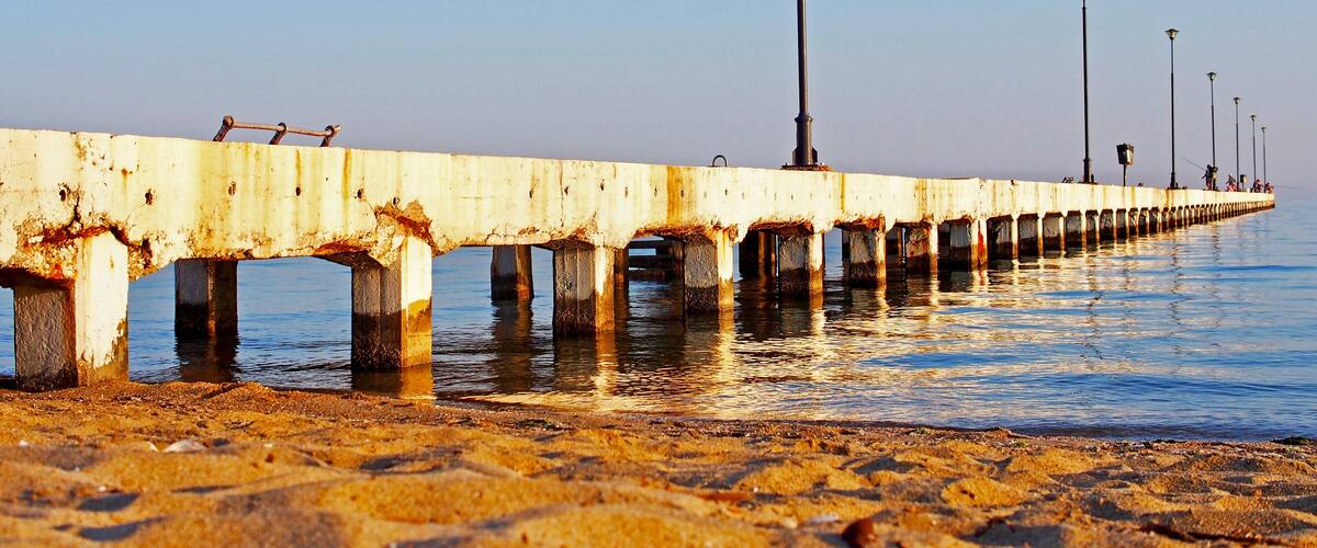 A long, rusted pier extending into calm waters with a clear sky.