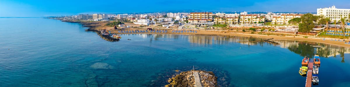 A coastal city with a clear blue sea, a rocky breakwater, and a row of colorful buildings along the shore.