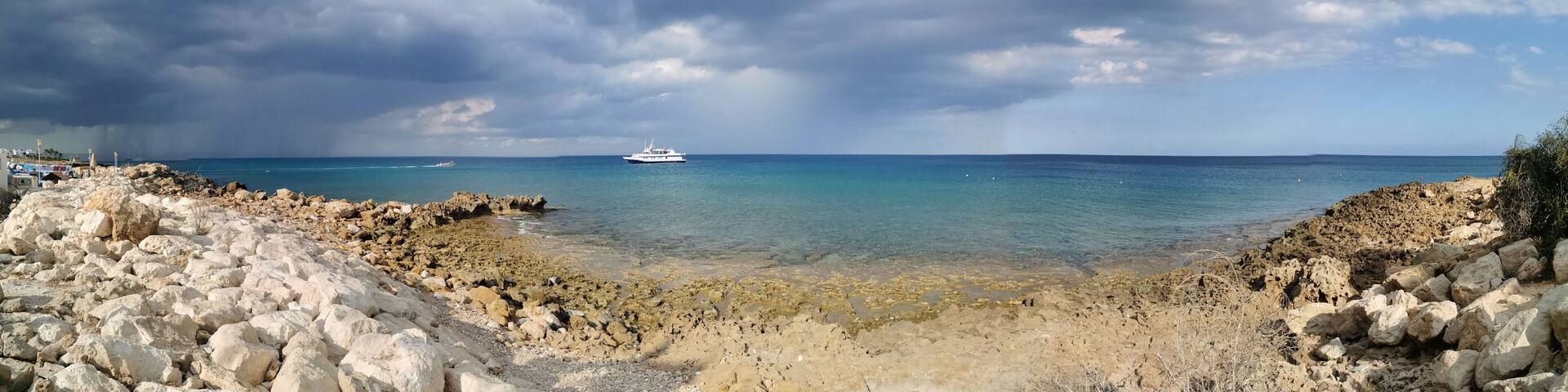 Panorama. The stone coast of the Mediterranean Sea, a white pleasure ship in the sea against a dramatic sky. with clouds.