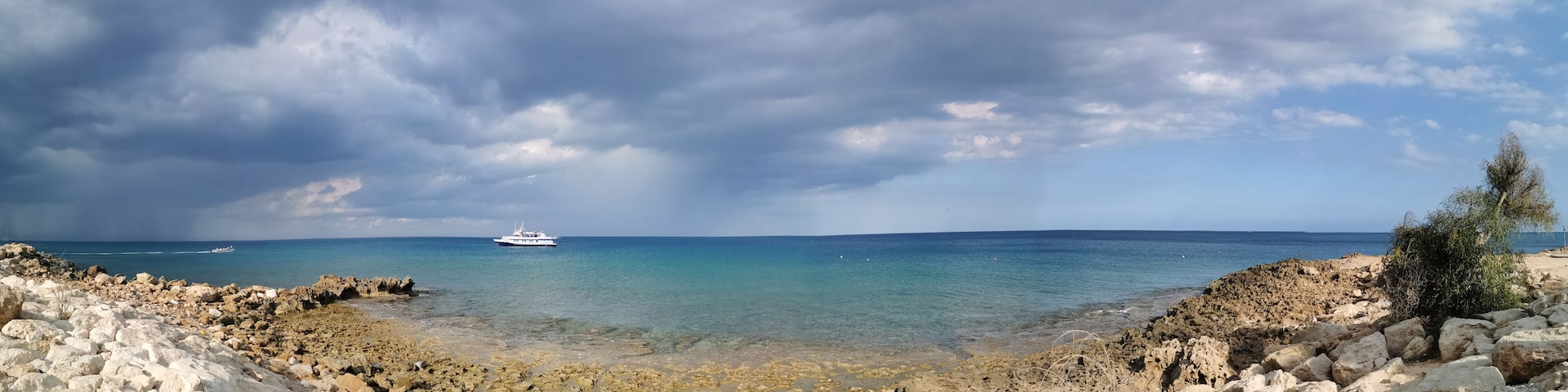 Uma costa rochosa com um barco ao longe e céu claro.