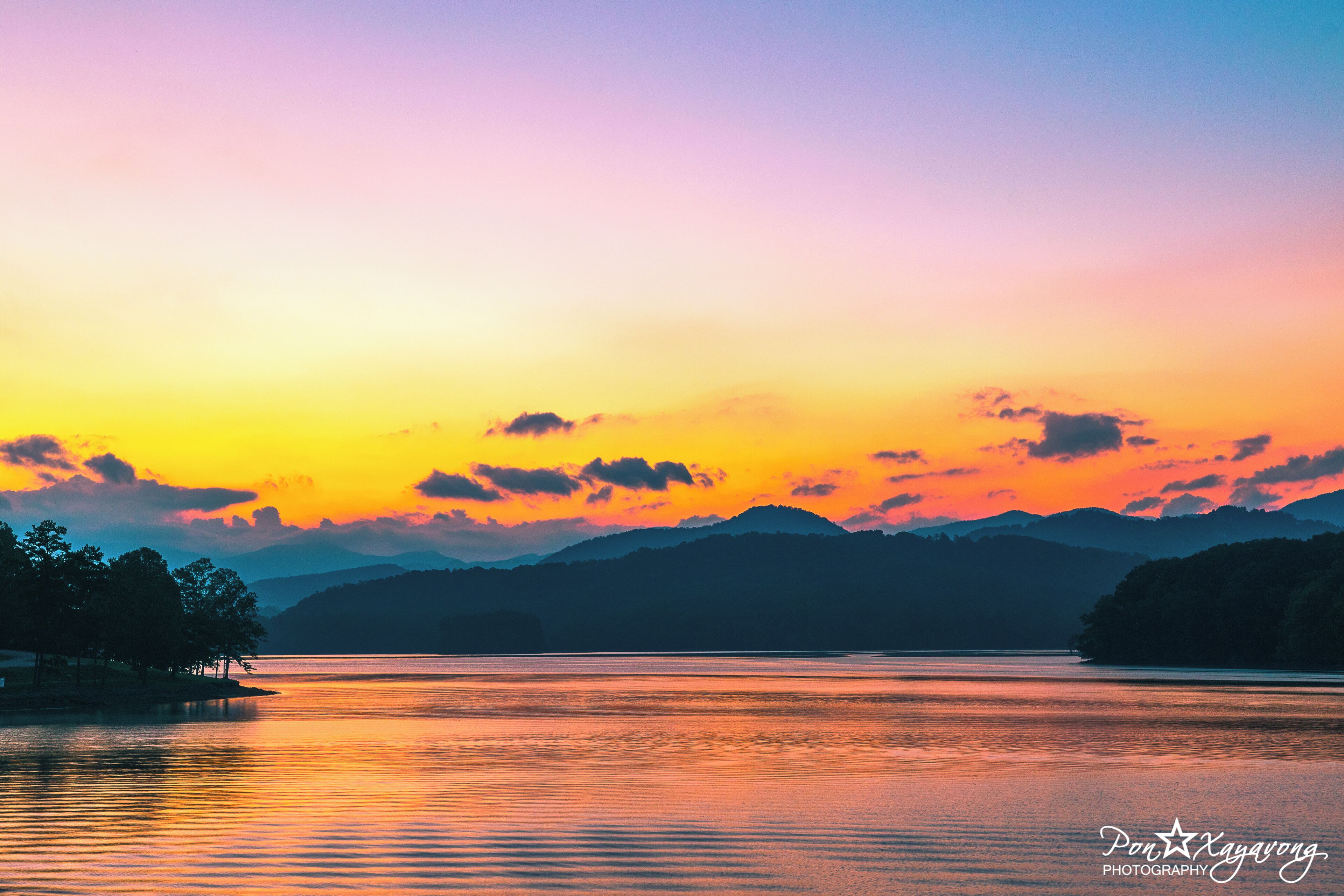A sunset over a calm lake with mountains in the background.