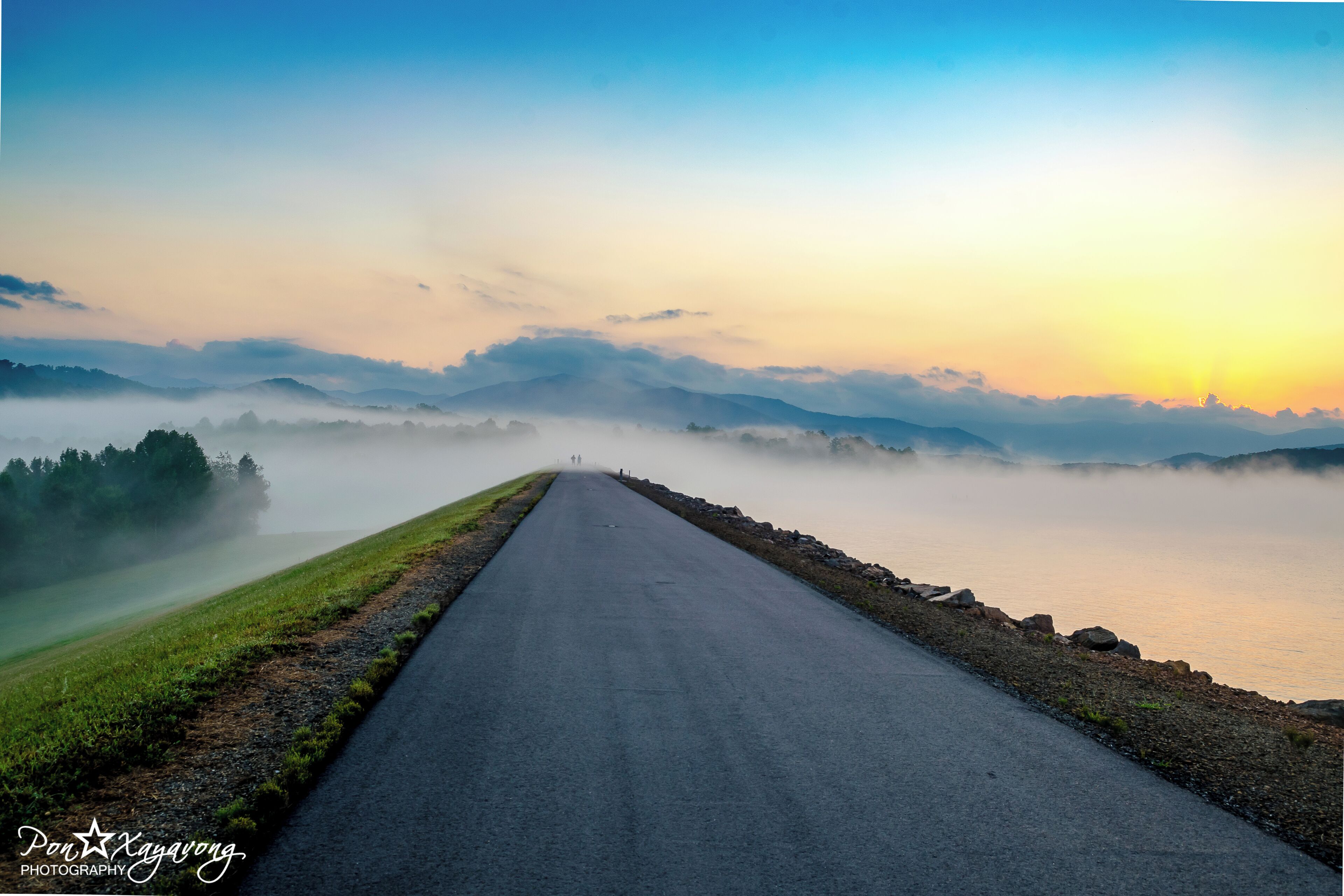 A road leading through a misty landscape with mountains in the background.