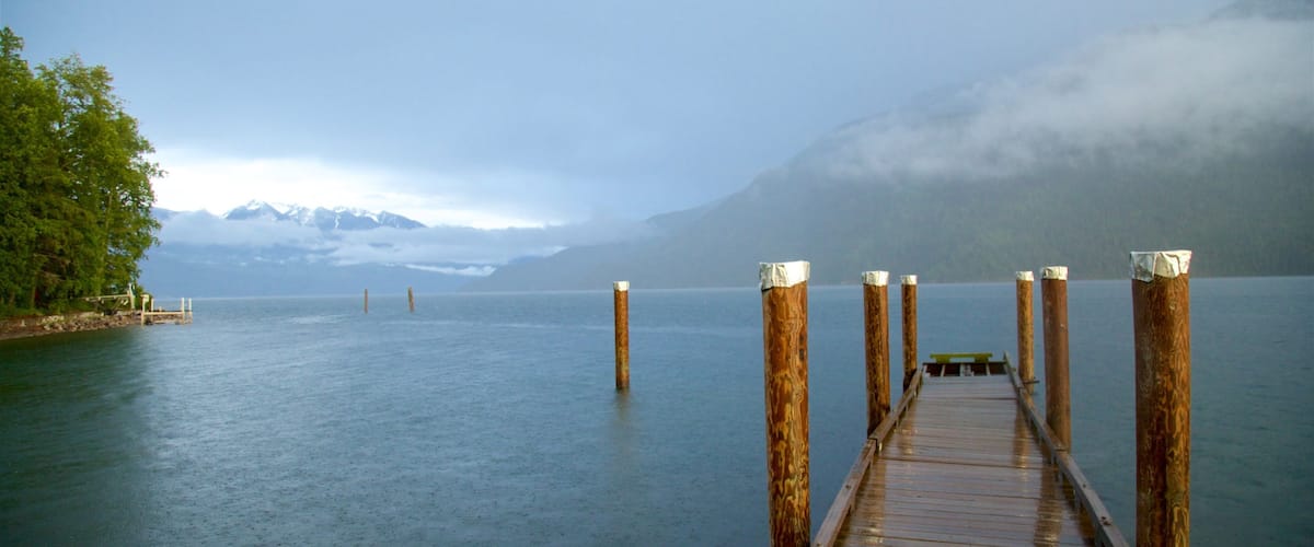 A wooden pier extending into calm waters with mountains in the background.