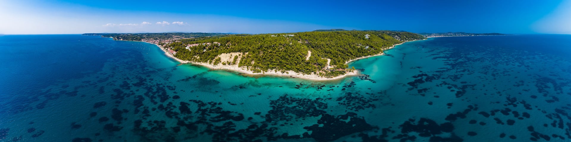 A coastal island with dense green vegetation, clear turquoise waters, and a sandy beach.