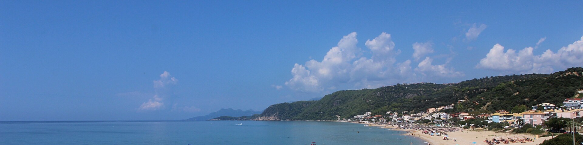 A beach with clear blue water, a sandy shore, and rows of umbrellas.