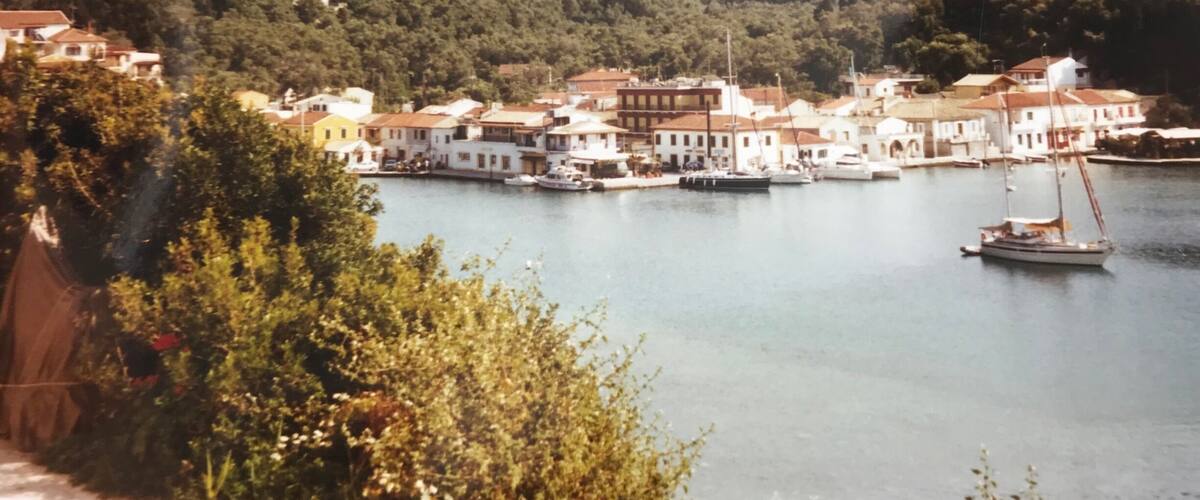 A coastal town with buildings along the waterfront, boats docked, and hills in the background.