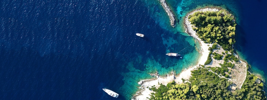 Vista aérea de una isla costera con aguas azul turquesa, una playa arenosa y vegetación exuberante.