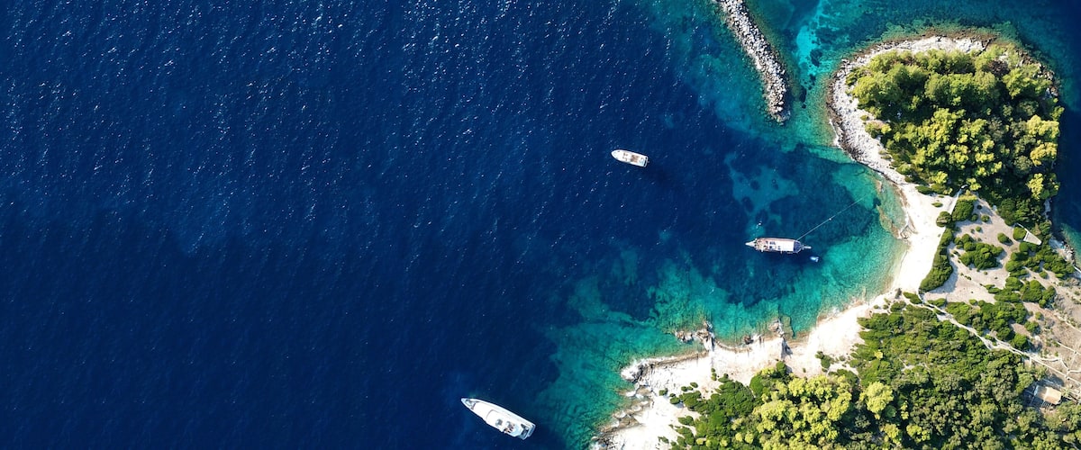 An aerial view of a coastal island with clear blue waters, a sandy beach, and lush greenery.