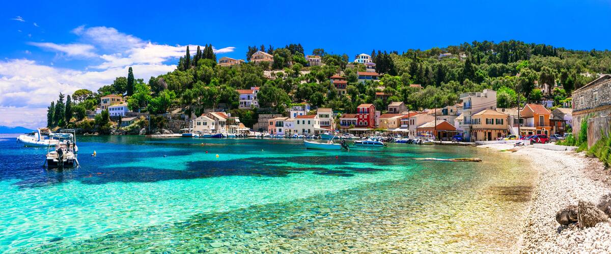 A coastal town with clear turquoise waters, boats, and colorful buildings on a hillside.