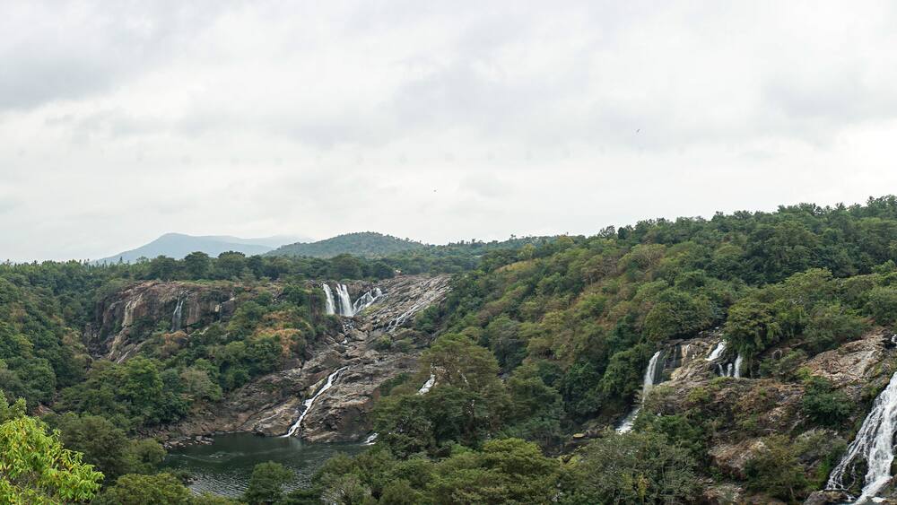 Eine gebirgige Landschaft mit mehreren Wasserfällen, die über steinige Klippen in einen Fluss stürzen.