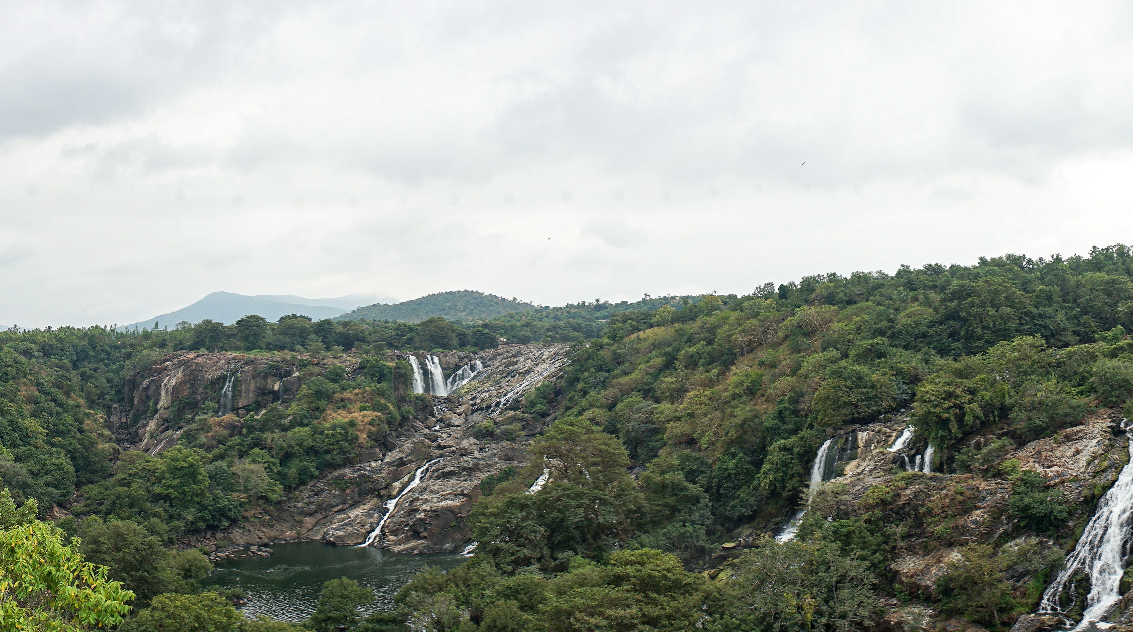 A mountainous landscape with multiple waterfalls cascading down rocky cliffs into a river below.