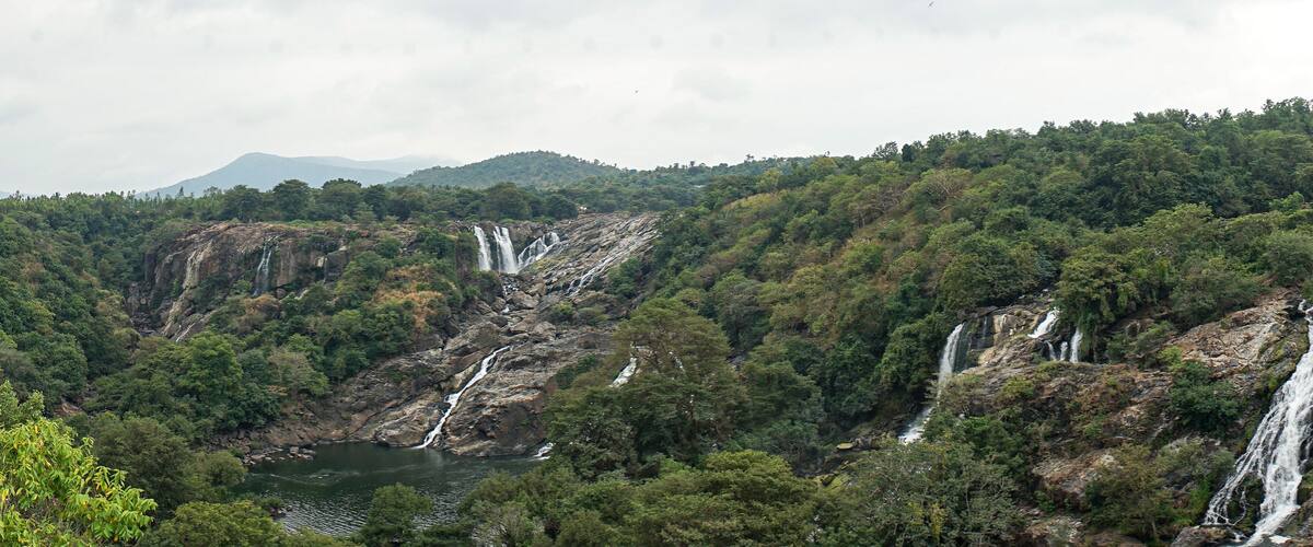 A mountainous landscape with multiple waterfalls cascading down rocky cliffs into a river below.
