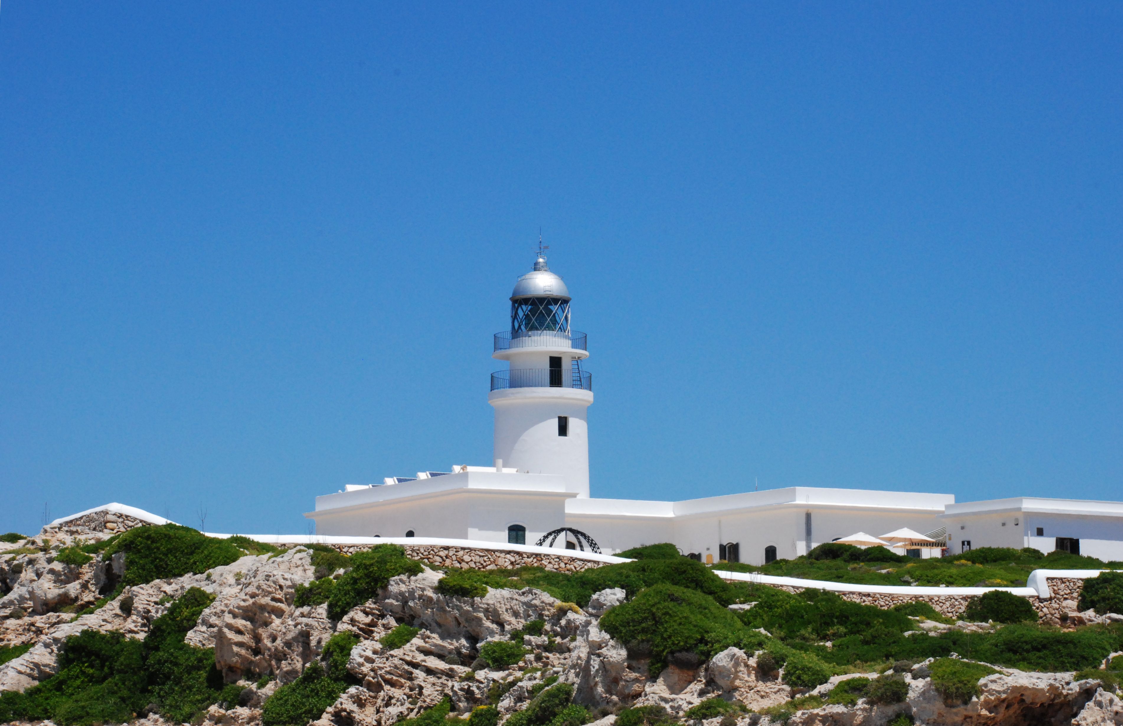 A white lighthouse with a blue dome and a white building with a flat roof.