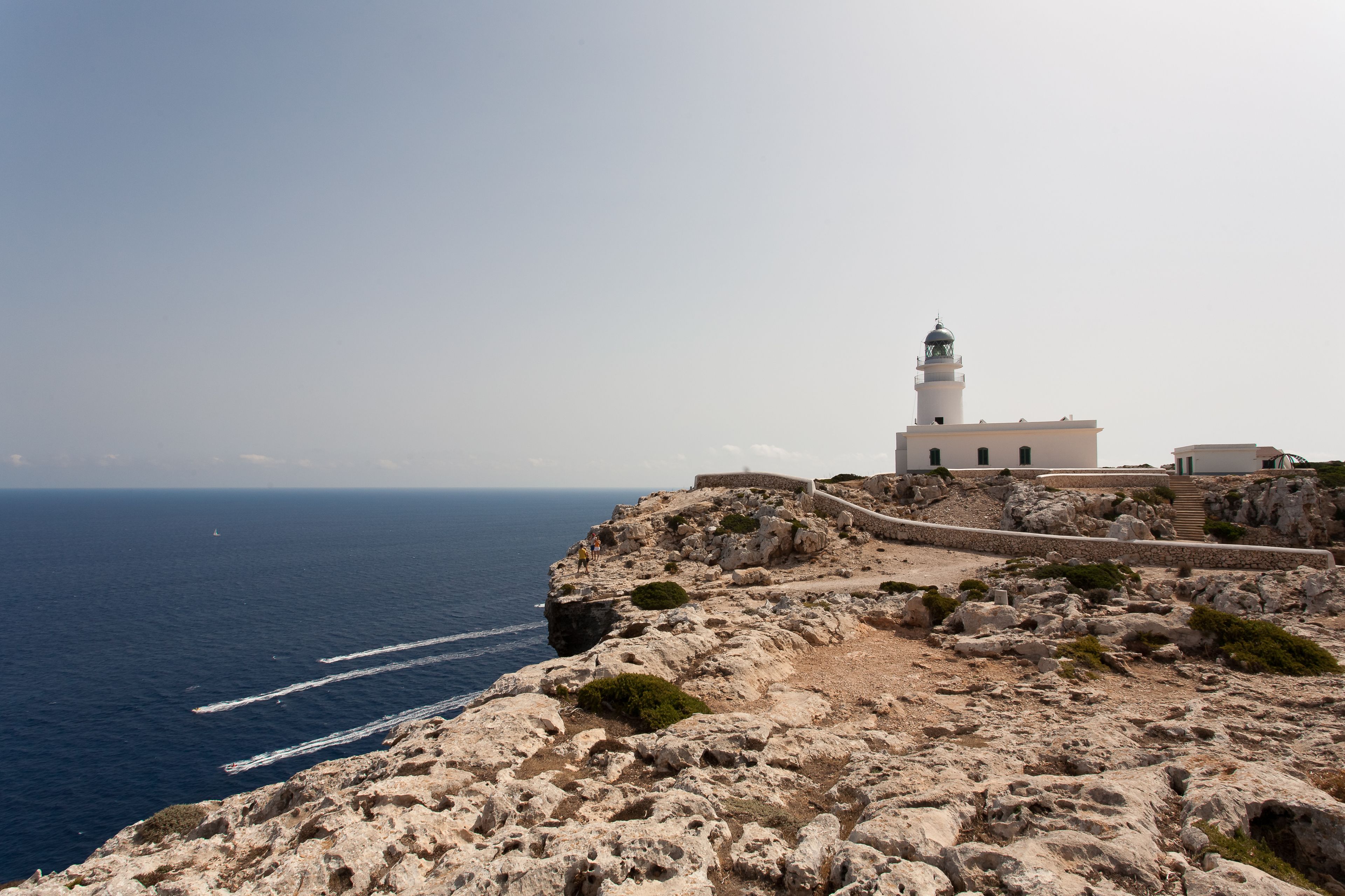 A coastal landscape with a lighthouse, rocky terrain, and a clear view of the sea.