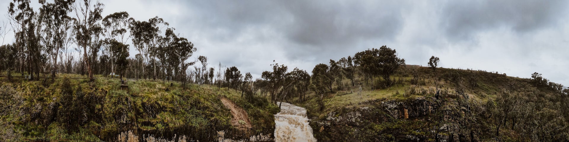 A waterfall cascading down a rocky cliff surrounded by dense greenery and trees.