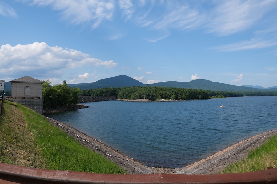 A river with a bridge, a small building, and mountains in the background.