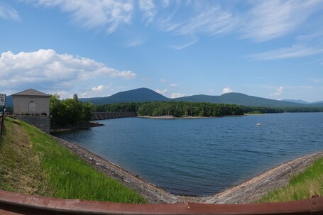 A river with a bridge, a small building, and mountains in the background.