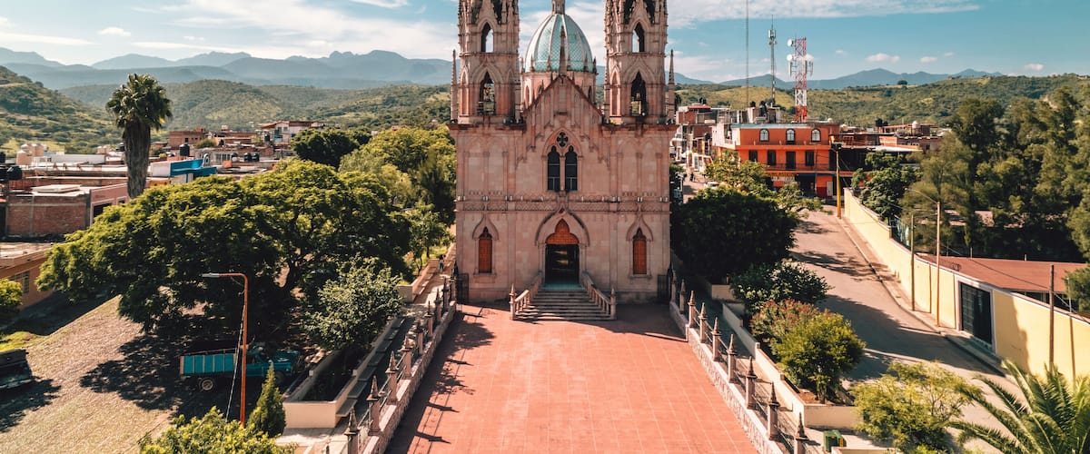 A historic church with two towers and a dome, surrounded by lush greenery and mountains.