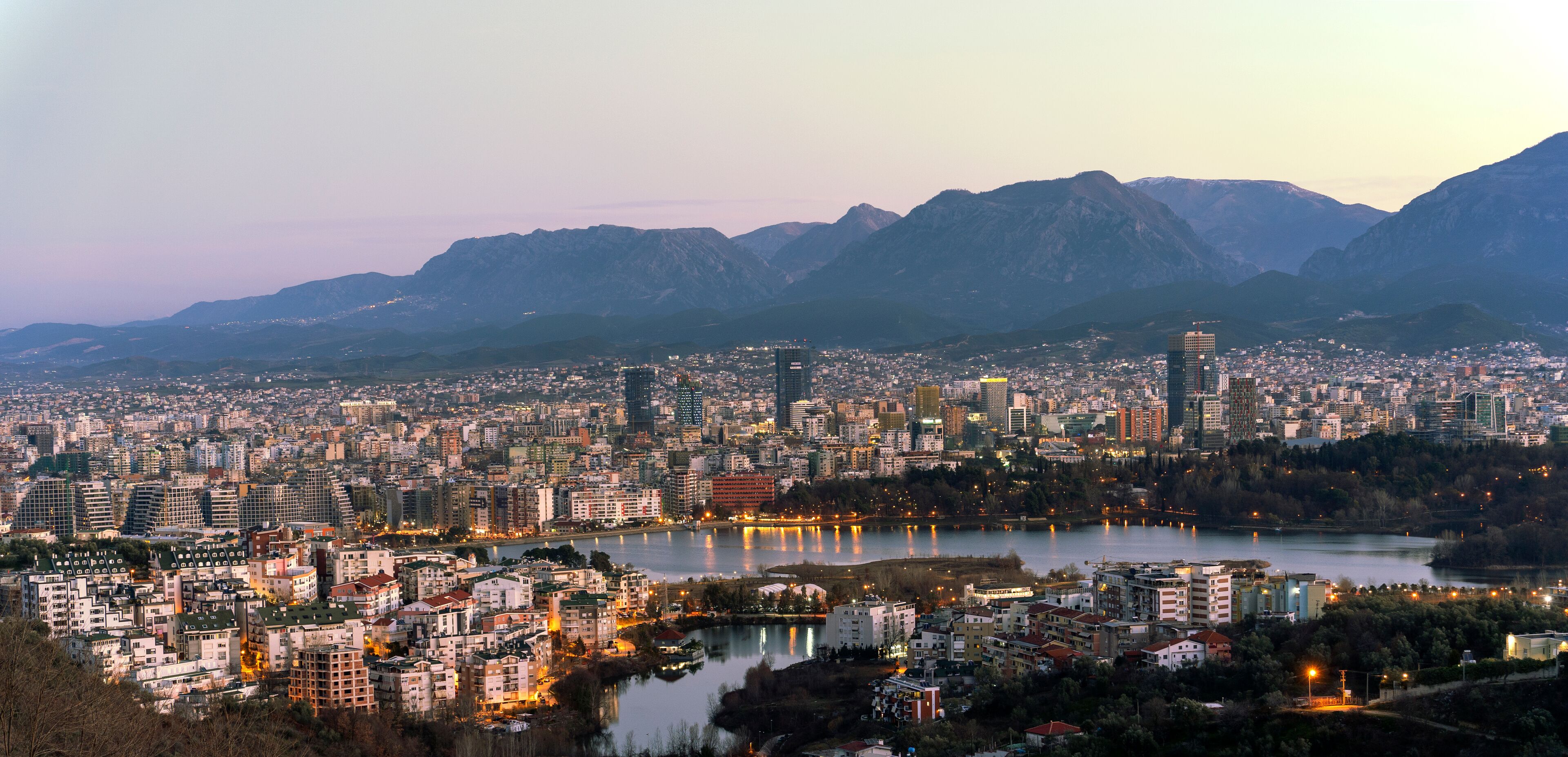 A cityscape with a river, mountains, and a variety of buildings.