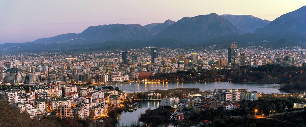A cityscape with a river, mountains, and a variety of buildings.