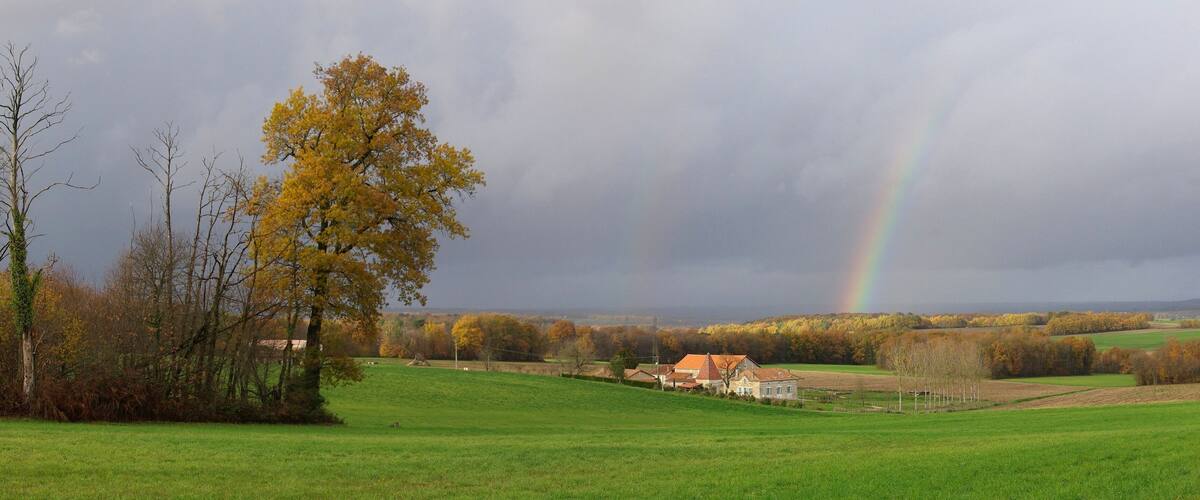 A rural landscape with a house, a rainbow, and autumn-colored trees.