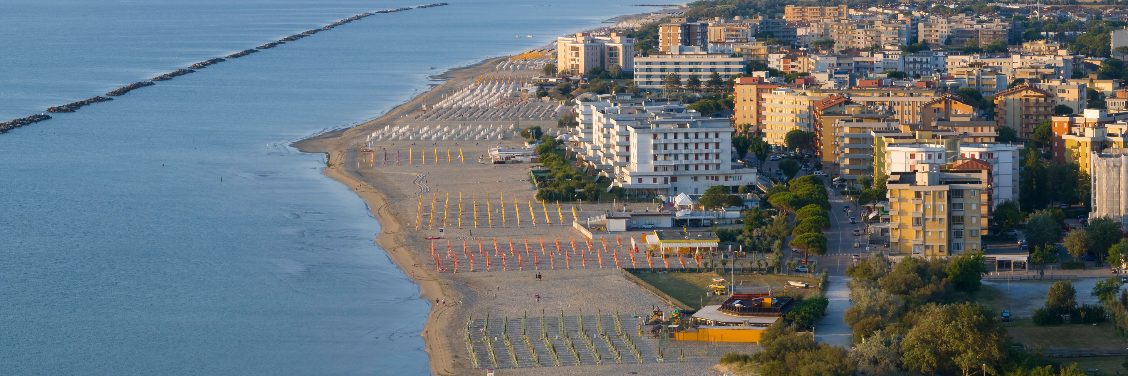 A coastal cityscape with a beach, buildings, and a breakwater.