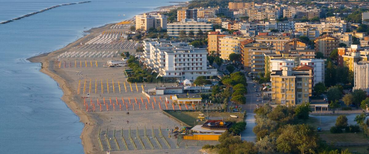 A coastal cityscape with a beach, buildings, and a breakwater.